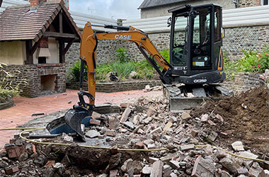 Accueil Pelle mécanique CASE CX50 réalisant la démolition d'une dalle en béton lors de travaux de terrassement et d'aménagement extérieur en Ille-et-Vilaine et Mayenne.